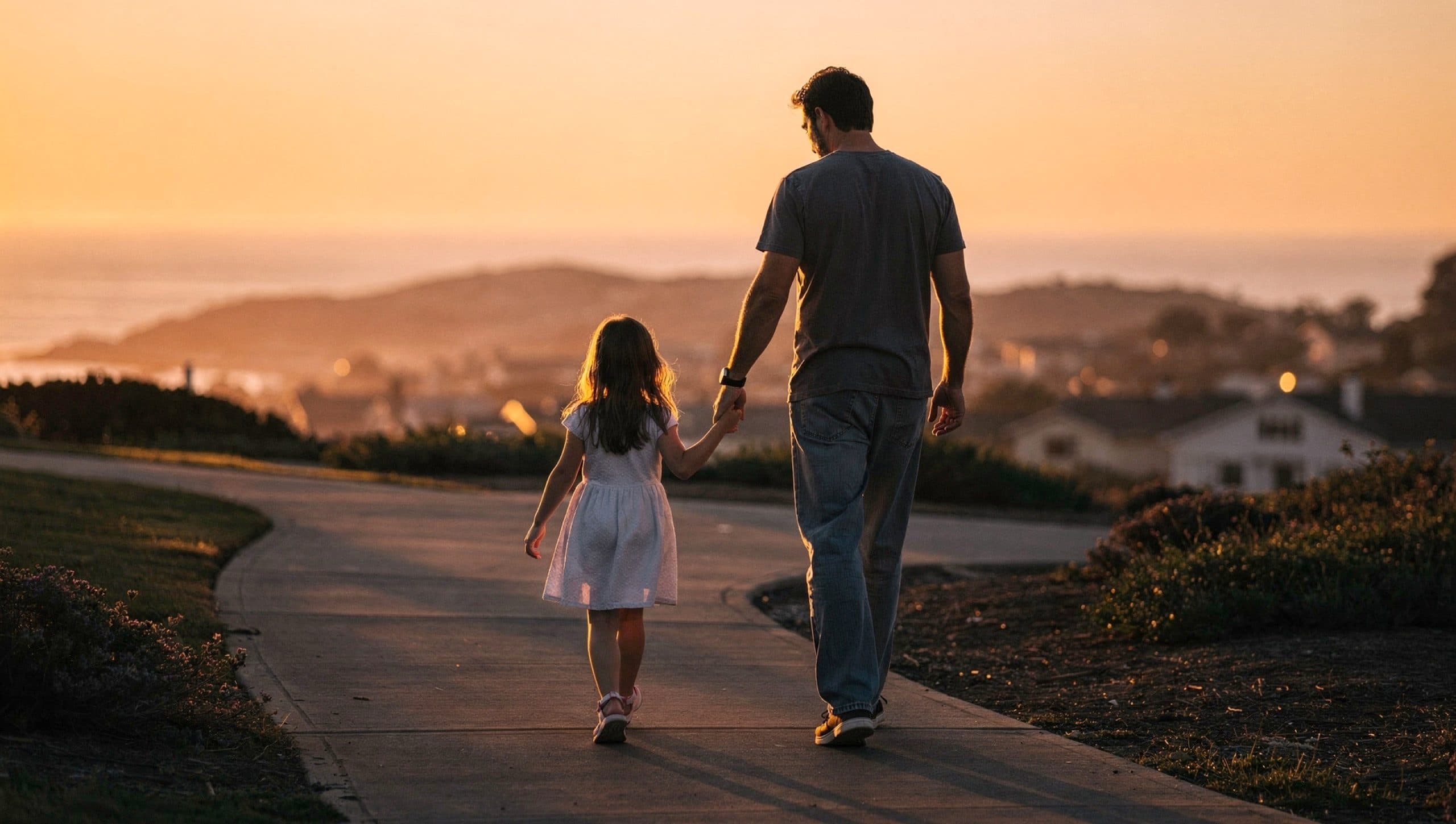 A father and daughter walking hand in hand against a warm sunset